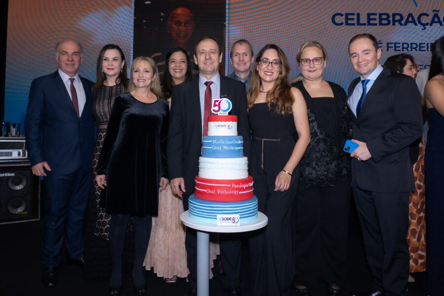 Profesionales de la Sociedade Brasileira de Estomatologia e Patologia Oral celebrando su 50.º aniversario alrededor de un pastel conmemorativo.