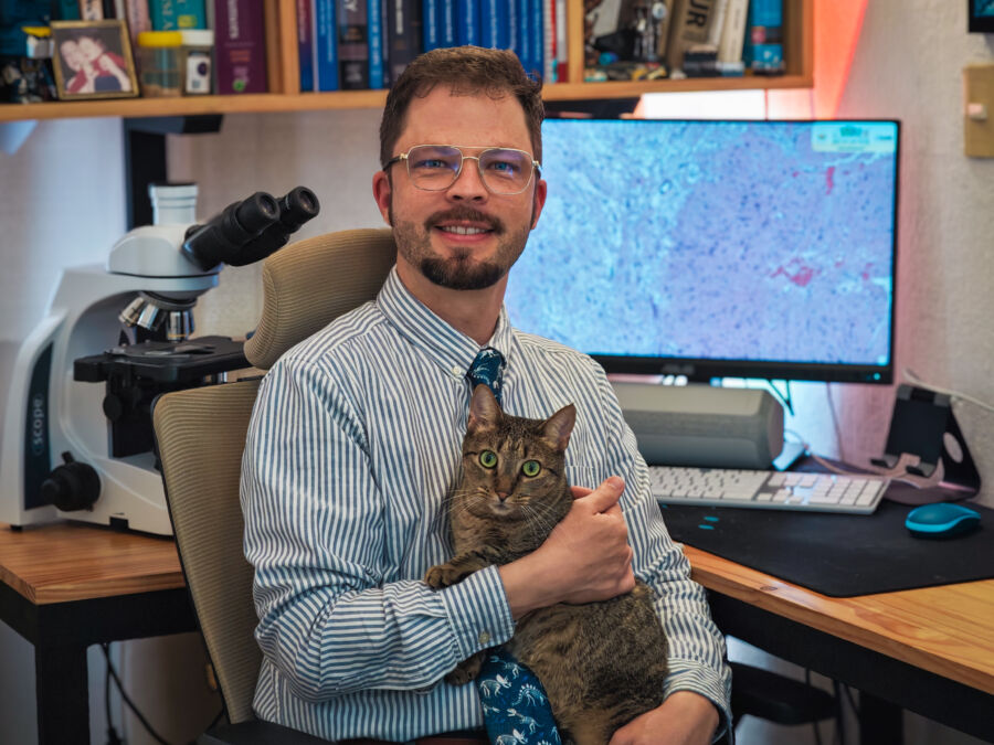 Dr. Roberto Gerber Mora, especialista en Patología y Medicina Bucal, en su espacio de trabajo junto a un microscopio y su gata.